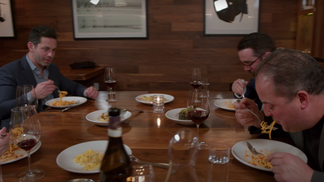 Captura del primer vídeo promocional del primer restaurante NFT del mundo, con los socios del proyecto en una mesa sin hule ni mantel, comiéndose unos espaghetti.