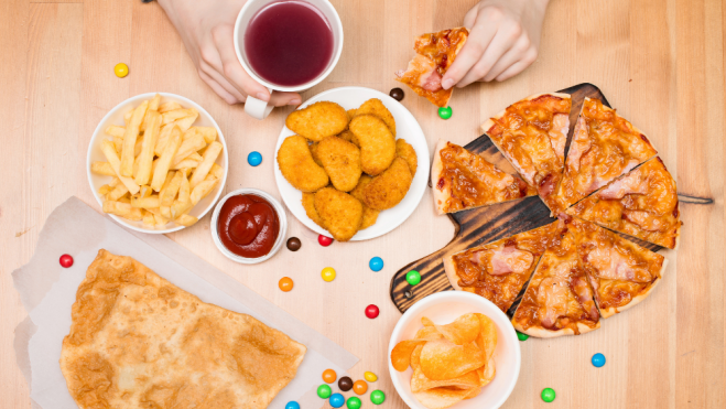 Niño comiendo patatas fritas, nuggets, pizza y otros alimentos considerados fast food / Foto: Canva