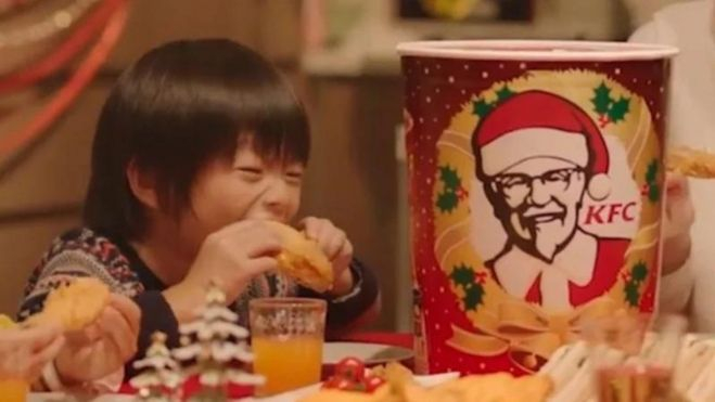 Un niño japonés come junto al típico barril de pollo frito navideño de KFC / Foto: Recorte de una publicidad