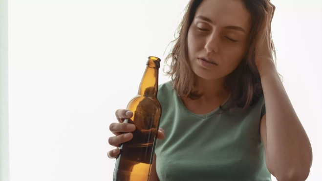 Una mujer con una botella de cerveza bajo los efectos del alcohol / Foto: Canva