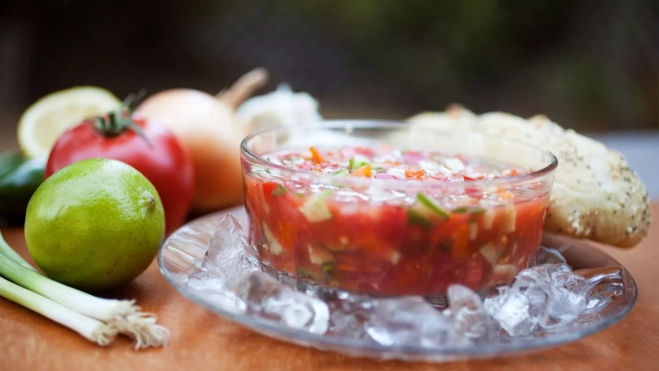 Vasito de gazpacho con verduras troceadas sobre un plato con hielo / Foto: Canva