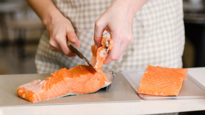 Cocinero extrayendo la espina de un filete de salmón / Foto: Canva