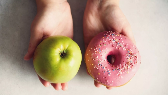 Persona debatiéndose entre comer una manzana o un donut / Foto: Canva