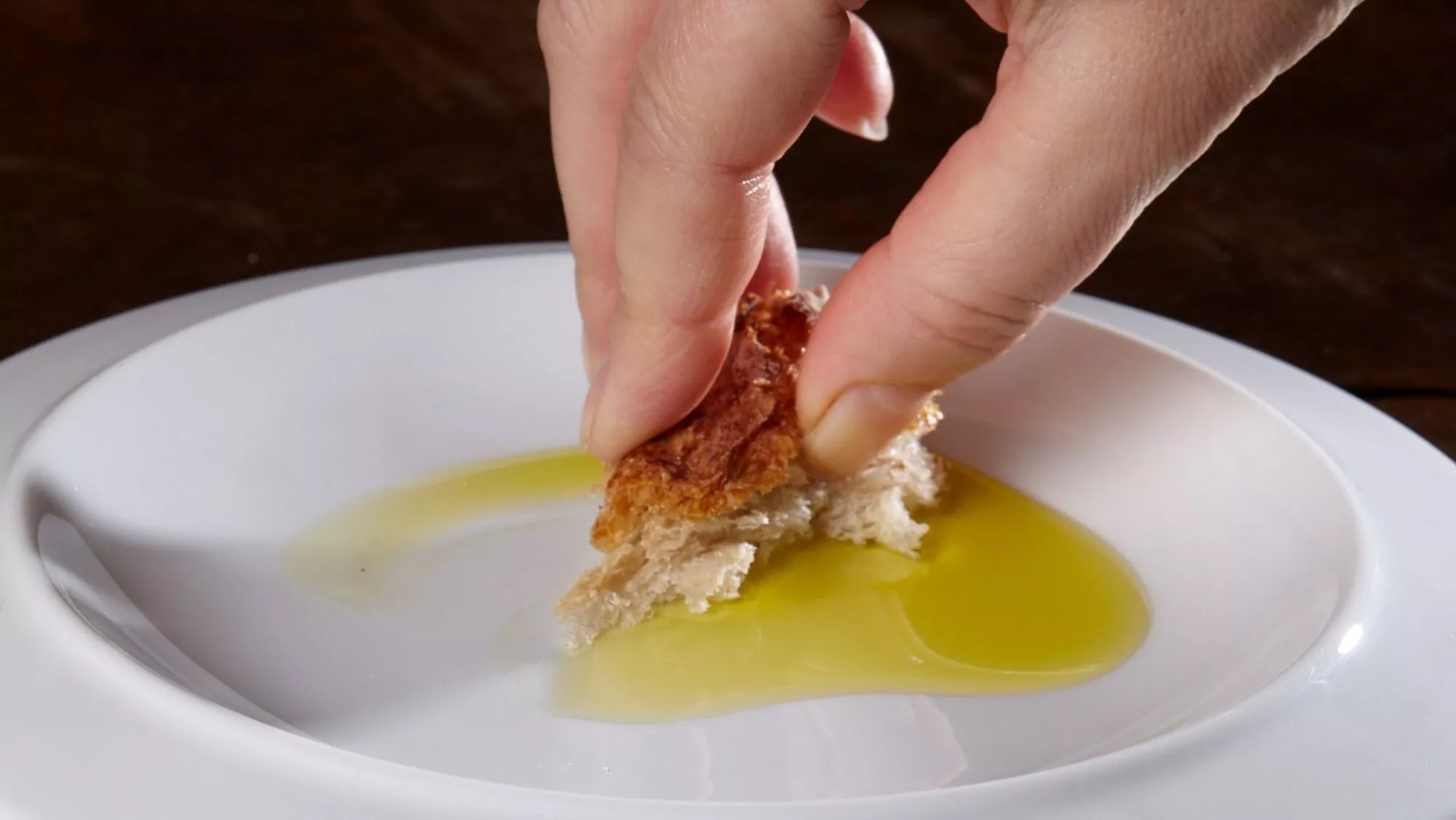 Mujer mojando pan en aceite de oliva virgen extra / Cedida