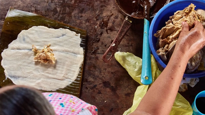 Mujer cocinando tamales con mole en un puesto callejero de Oaxaca (México) / Canva