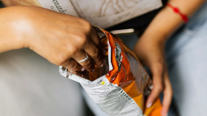 Adolescente comiendo una bolsa de snacks / Canva