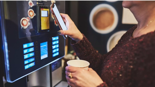 Mujer comprando un café o bebida caliente en una máquina / Canva
