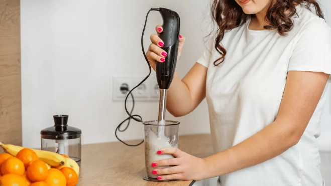Mujer prepara un smoothie con una batidora de mano / CANVA