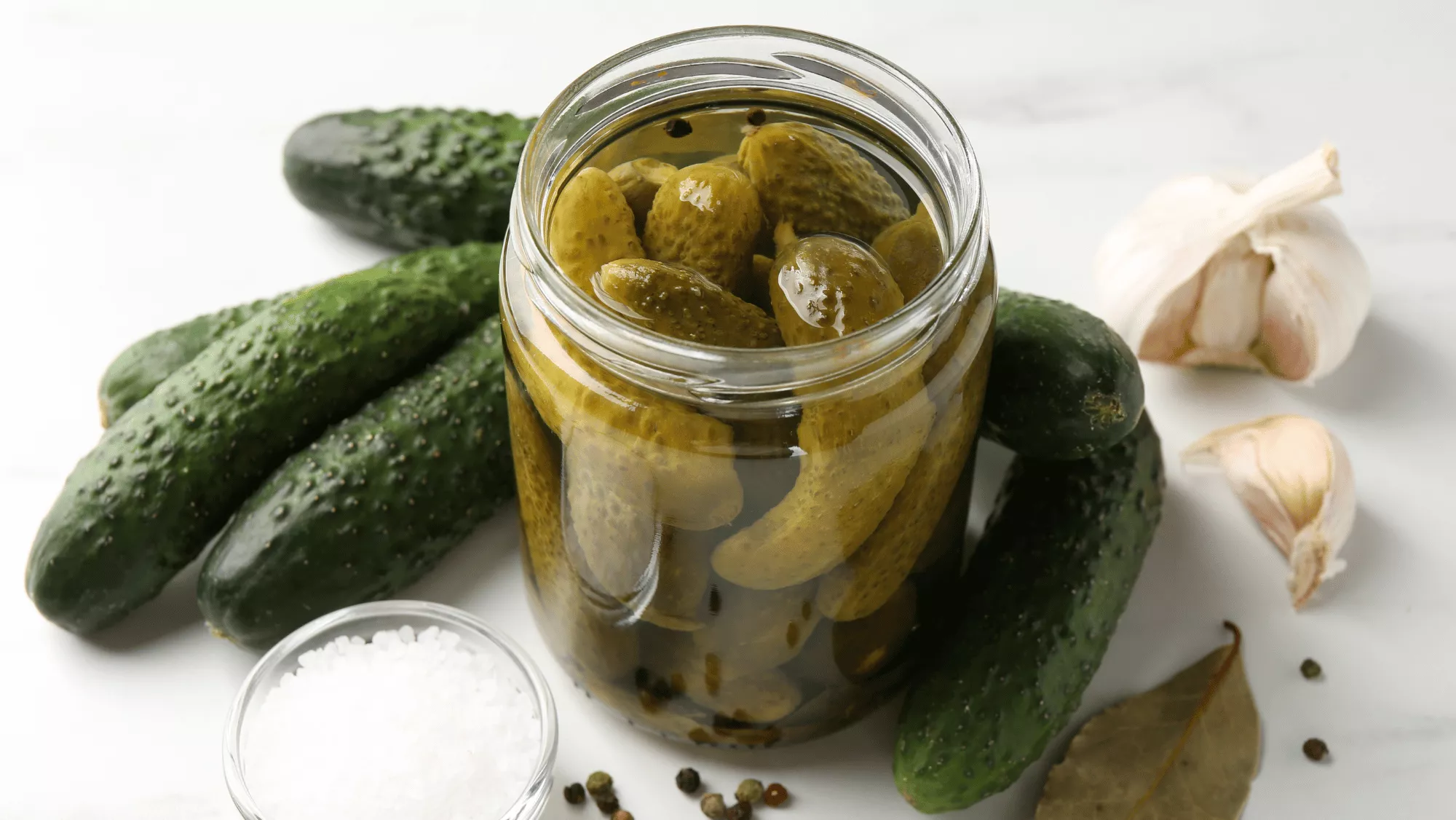 Frasco de pepinillos en salmuera acompañado de pepinos frescos, ajo y especias / CANVA