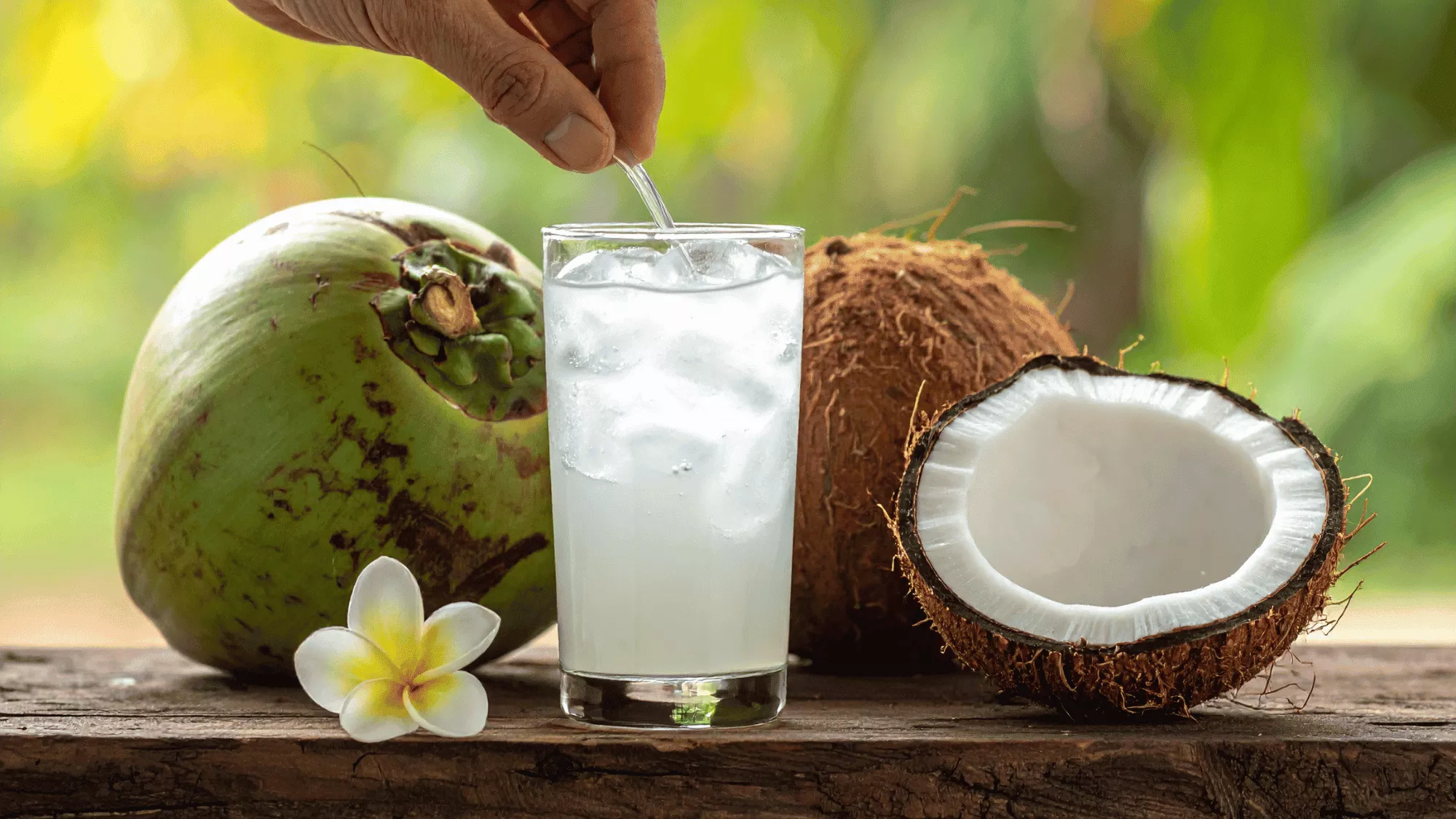 Vaso de agua de coco delante de varios cocos | Canva