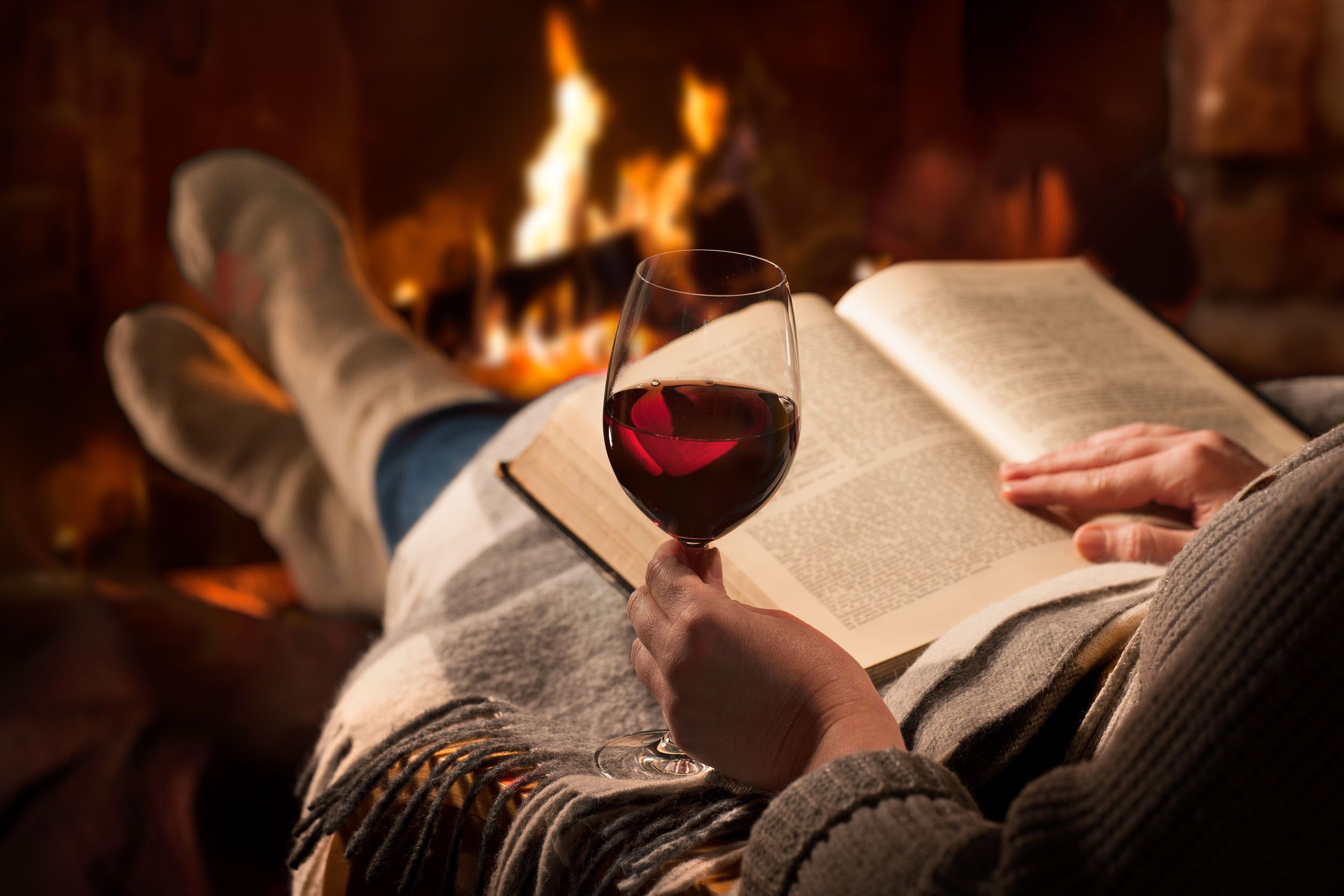 56702272 - woman resting with glass of red wine and book near fireplace